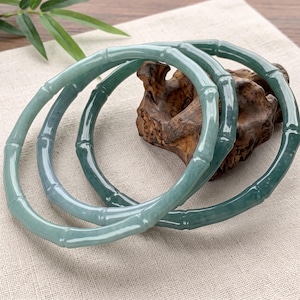 May include: Two circular bangles crafted from smooth, translucent green stone. Each bangle features a segmented design that mimics the appearance of natural bamboo stalks, with raised nodes spaced evenly around the circumference of the rings.