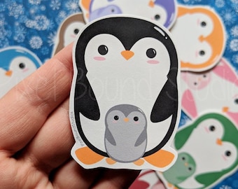 以下が含まれることがあります： カラフルなペンギンのステッカーのコレクション。メインのステッカーは、小さな灰色のペンギンと一緒に白黒のペンギンを特徴としています。他のステッカーには、青、紫、オレンジ、ピンク、緑のペンギンが含まれています。背景は青い雪の結晶模様です。