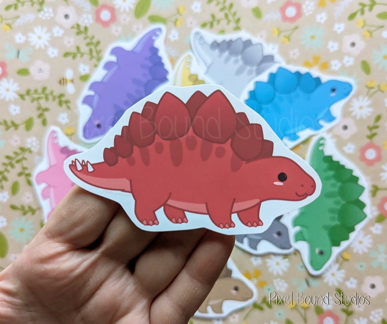Puede incluir: Un conjunto de pegatinas de dinosaurios de colores que incluyen un dinosaurio rojo, morado, azul, verde y gris. Los dinosaurios est&aacute;n todos en un estilo de dibujos animados y tienen una expresi&oacute;n amigable. Las pegatinas son perfectas para agregar un toque de fantas&iacute;a a cualquier proyecto.