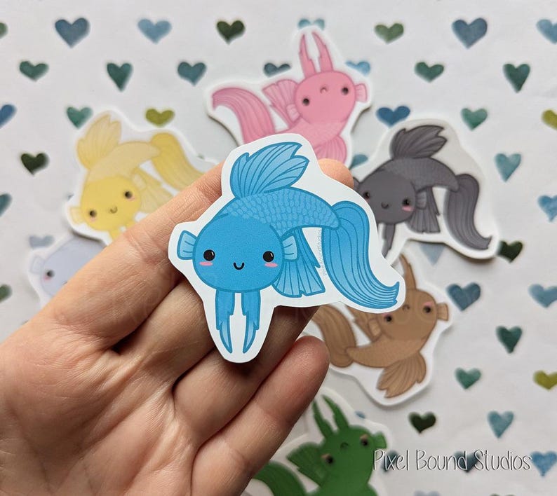 Pode incluir: Um conjunto de adesivos de peixes coloridos com um peixe betta azul, um axolotl rosa, um peixe dourado amarelo, um peixe-anjo preto e branco e um guppy castanho e branco. Os adesivos est&atilde;o em um fundo branco com cora&ccedil;&otilde;es azuis e verdes.
