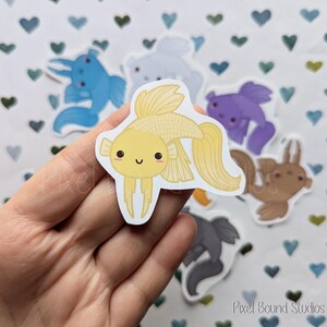 Pode incluir: Um conjunto de adesivos de peixes coloridos com rostos de desenhos animados fofos. Os adesivos apresentam um peixe amarelo com um grande sorriso, um peixe azul com um pequeno sorriso, um peixe roxo com um pequeno sorriso, um peixe marrom com um pequeno sorriso e um peixe cinza com um pequeno sorriso.