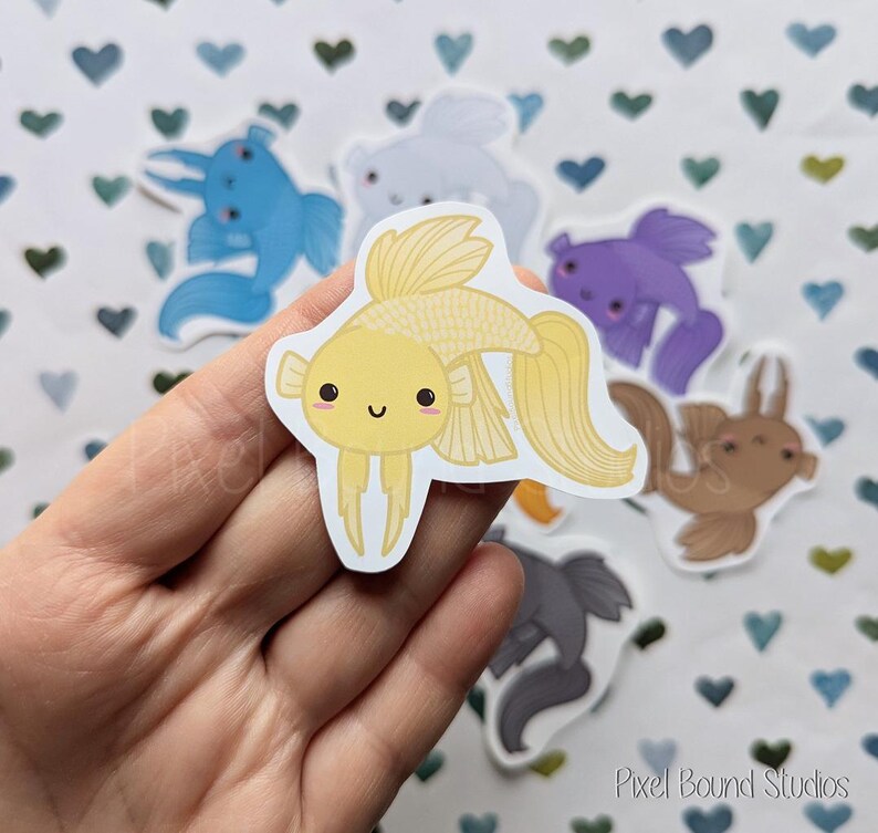 Pode incluir: Um conjunto de adesivos de peixes coloridos com rostos de desenhos animados fofos. Os adesivos apresentam um peixe amarelo com um grande sorriso, um peixe azul com um pequeno sorriso, um peixe roxo com um pequeno sorriso, um peixe marrom com um pequeno sorriso e um peixe cinza com um pequeno sorriso.