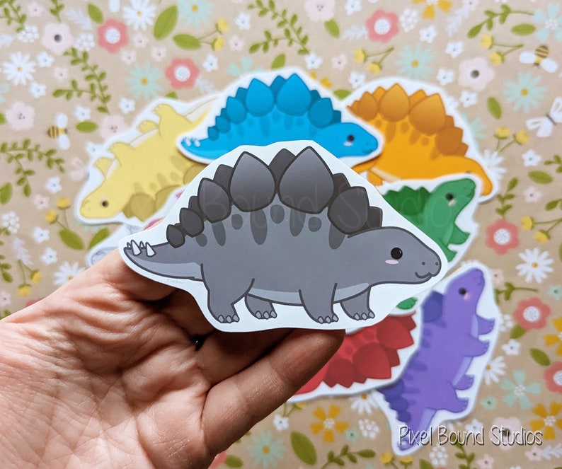 Puede incluir: Un conjunto de pegatinas de dinosaurios de colores que representan diferentes especies, incluyendo un estegosaurio, un anquilosaurio y un triceratops. Las pegatinas son perfectas para a&ntilde;adir un toque divertido y caprichoso a cualquier proyecto.