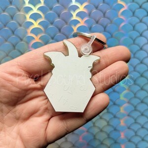 May include: White acrylic keychain shaped like a Dungeons and Dragons die with a 4-sided design. The keychain has a silver metal ring attached.