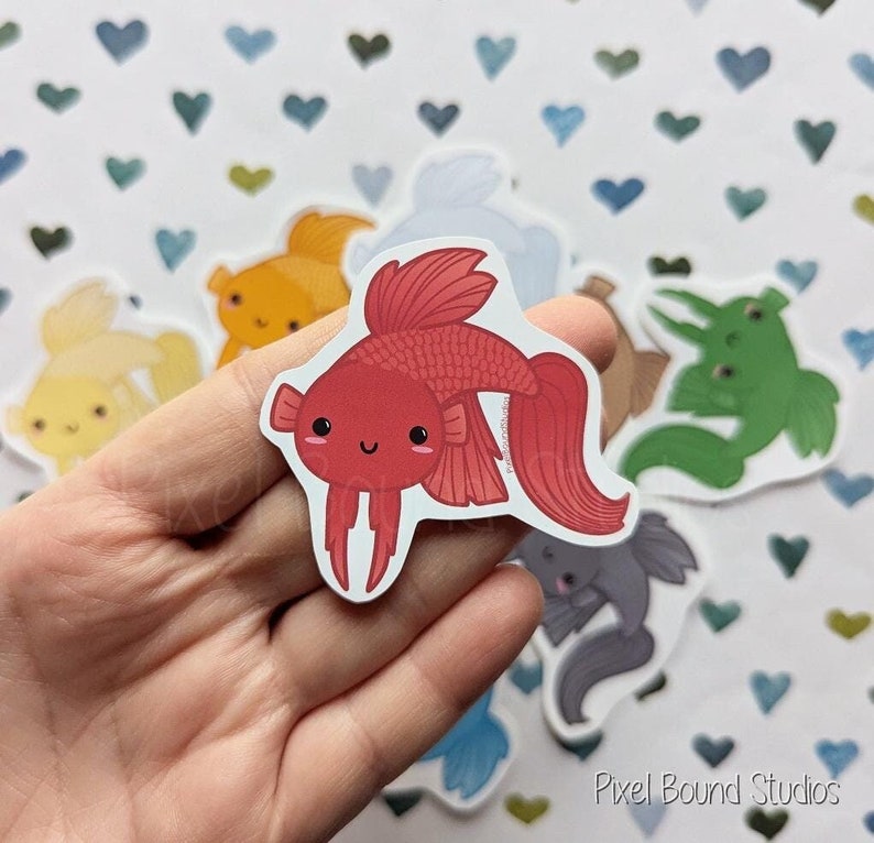 Pode incluir: Um conjunto de adesivos de peixes coloridos com rostos de desenhos animados fofos. Os adesivos apresentam um peixe betta vermelho, um peixe dourado amarelo, um sapo verde, um peixe azul, um peixe cinza e um peixe branco. Os adesivos est&atilde;o em um fundo branco com um padr&atilde;o de cora&ccedil;&otilde;es.