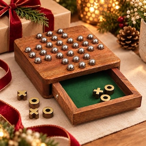 May include: A wooden board game featuring a grid of silver metal spheres on the top surface and a pull-out drawer containing brass-colored X and O game pieces. The interior of the drawer is lined with green felt for playing tic-tac-toe.