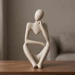 Könnte beinhalten: Eine beige Skulptur einer sitzenden Figur mit gesprenkelter Textur. Die Figur ist in einer ruhenden Pose dargestellt, wobei eine Hand das Kinn berührt und der andere Arm auf dem Schoß ruht, was eine offene, abstrakte Form mit geschwungenen Linien ergibt.