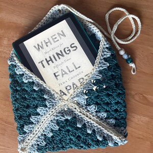 May include: A crocheted envelope-style sleeve in dark teal and light gray yarn, featuring a cream-colored border and a matching drawstring with three decorative beads. An e-reader is inside, displaying the book cover When Things Fall Apart.