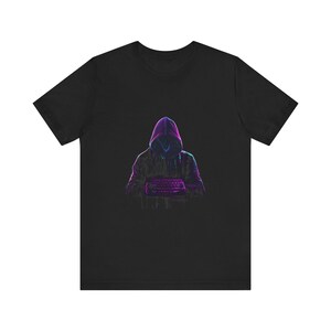 May include: A black short-sleeved t-shirt featuring a graphic print of a hooded figure in a dark silhouette. The figure is illuminated by vibrant neon purple and blue outlines, appearing to type on a keyboard held in front of the chest.