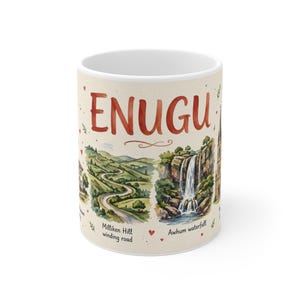 May include: A white ceramic mug featuring the text ENUGU in large red letters. The design includes watercolour-style illustrations of the Milliken Hill winding road and Awhum waterfall, accented with small red hearts and green foliage details.