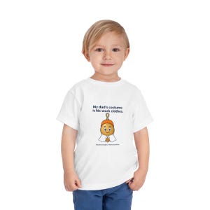 May include: A white short-sleeved t-shirt featuring a graphic of a cartoon acorn wearing a ghost costume. The text reads: My dad's costume is his work clothes. Honest trades. Honest prices. The shirt is made of a plain white fabric material.