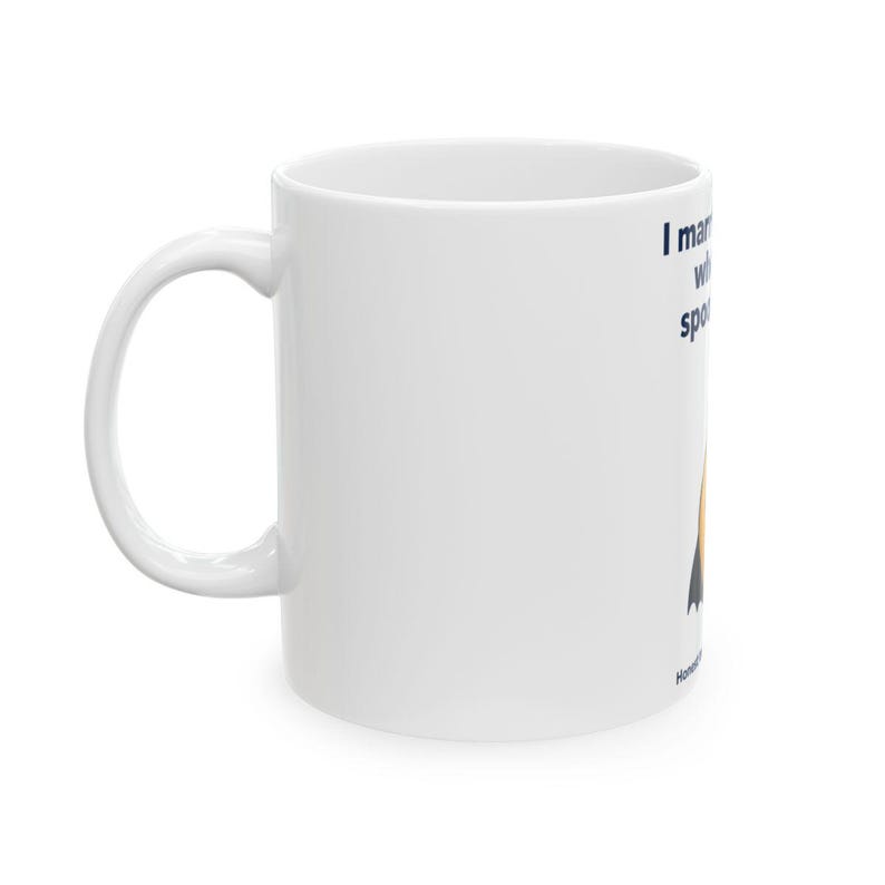 May include: A white ceramic mug featuring a dark blue text graphic that reads I married a witch and she spotted me. Below the text is a stylised orange pumpkin illustration with a black witch hat on top. The mug has a curved handle on the left side.