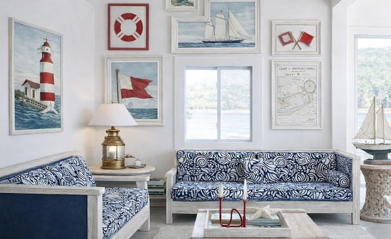 May include: A living room set featuring a sofa and armchair with white and blue patterned cushions, a brass nautical lamp, and a gallery wall displaying framed artwork of lighthouses, sailboats, signal flags, and a nautical chart on white walls.