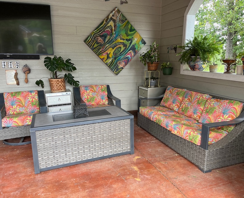 May include: A patio furniture set featuring a rectangular coffee table with a gray woven base and a dark top, two armchairs, and a three-seat sofa. All seating pieces have dark frames and cushions with a vibrant, multi-colored tropical leaf pattern.