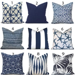 May include: A collection of nine square throw pillows featuring various blue and white patterns, including tie-dye grids, solid navy, intricate geometric designs, textured stripes, vertical stripes, starfish prints, floral motifs, and palm leaf patterns.
