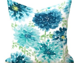 May include: A white throw pillow with a blue and teal floral pattern. The flowers are watercolor style and have a soft, faded look.
