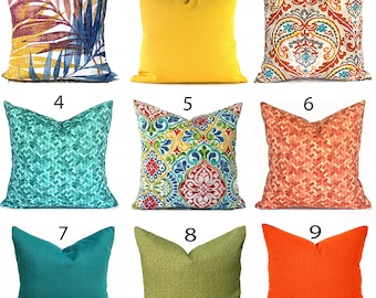 May include: A collection of nine square throw pillows featuring various designs: a tropical leaf print, solid yellow, orange and blue paisley, teal geometric weave, multi-colored floral pattern, orange geometric weave, solid teal, solid green, and solid orange.