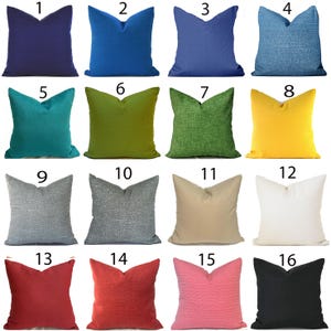May include: A collection of sixteen square throw pillows in various solid colors. The colors include shades of blue, green, yellow, gray, red, pink, and black. The pillows have a textured appearance, with some featuring a woven or ribbed design.