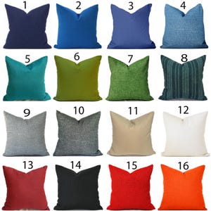 May include: A collection of sixteen square throw pillows arranged in a grid, featuring a variety of solid colors and textured fabrics including navy, royal blue, teal, olive green, grey, charcoal, beige, white, red, black, and bright orange.
