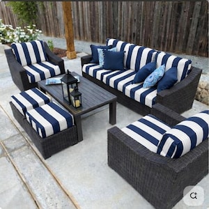 May include: An outdoor patio furniture set featuring a sofa, two armchairs, and two ottomans with dark brown wicker frames and navy blue and white striped cushions. A rectangular dark wood coffee table sits in the center with two lanterns.