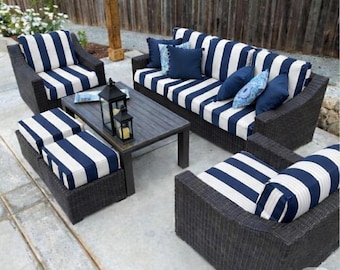 May include: An outdoor patio furniture set featuring a sofa, two armchairs, and two ottomans with dark brown wicker frames and navy blue and white striped cushions. A rectangular dark wood coffee table sits in the center with two lanterns.