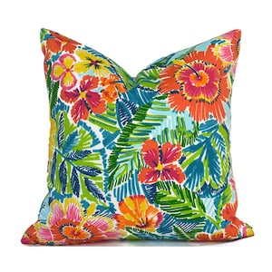May include: A colorful throw pillow with a tropical floral pattern. The pillow features bright pink, orange, yellow, and blue flowers on a white background. The flowers are surrounded by green leaves.