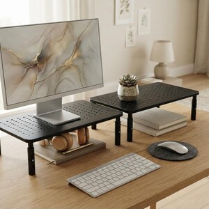May include: Two black monitor stands with perforated surfaces and adjustable legs. One stand supports a computer monitor with an abstract gold and white marble pattern on the screen. The other stand holds a small potted succulent plant.