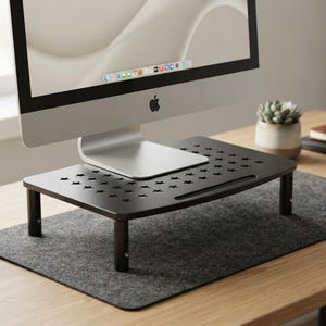 May include: A black monitor stand with a rectangular platform featuring a repeating star-shaped cutout pattern. The stand is supported by four adjustable cylindrical legs and holds a silver computer monitor on its flat surface.