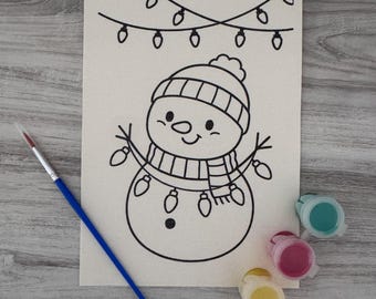 Op de afbeelding: Een rechthoekig canvas met een zwarte lijntekening van een sneeuwpop met een muts en sjaal, versierd met lichtsnoeren. Een blauwe kwast en vier kleine ronde verfpotjes in de kleuren groenblauw, roze, geel en wit zijn inbegrepen.