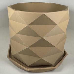 May include: A light tan cylindrical planter featuring a geometric, faceted exterior surface with triangular patterns. The planter sits on a matching, shallow, hexagonal-shaped saucer base, creating a cohesive unit for holding small plants or decorative items.