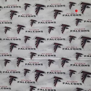 May include: White fabric with a repeating pattern of the Atlanta Falcons logo. The logo is red, black, and white and features a falcon's head with a wing outstretched.