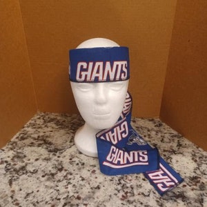 Könnte beinhalten: Ein blaues und weißes Stirnband mit dem aufgedruckten Wort "Giants". Das Stirnband wird auf einem weißen Mannequin-Kopf getragen. Das Stirnband ist auch um den Hals des Mannequins gebunden.