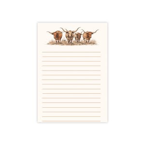 May include: A rectangular notepad featuring a cream-colored background with horizontal light brown lines. At the top, there is a detailed illustration of four brown longhorn cattle standing in a field of dry grass, facing forward.