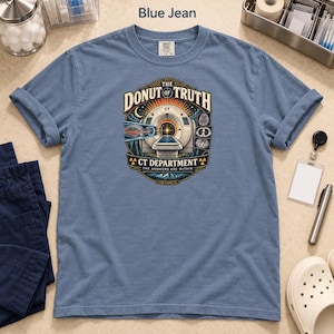 May include: A blue jean colored short-sleeve t-shirt featuring a graphic print of a CT scanner. The text reads THE DONUT OF TRUTH, CT DEPARTMENT, and THE ANSWERS ARE WITHIN. The design includes medical imaging icons, radiation symbols, and a forest scene.