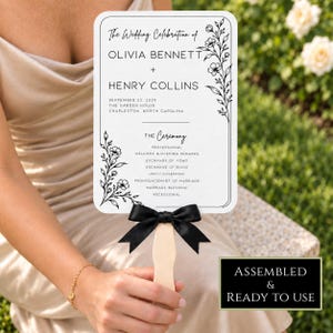 May include: A rectangular wedding program fan featuring black text and floral illustrations on a white background. The text reads The Wedding Celebration of Olivia Bennett and Henry Collins, September 22, 2029, The Garden House, Charleston, North Carolina.