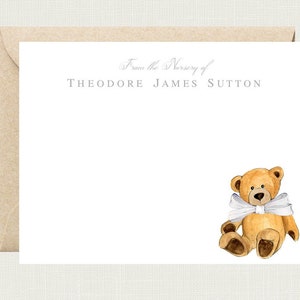 Peut inclure: Une carte blanche avec une enveloppe brune. La carte porte le texte "From the Nursery of Theodore James Sutton" en gris. Une illustration aquarelle d'un ours en peluche brun avec un n&oelig;ud blanc se trouve dans le coin inf&eacute;rieur droit.