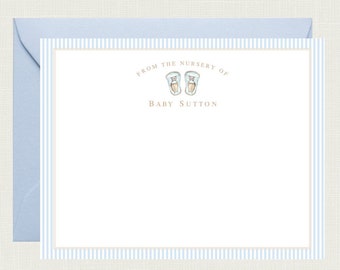 May include: A white card with blue and white stripes around the border. The card says "From the nursery of Baby Sutton" with a pair of blue baby shoes above the text.