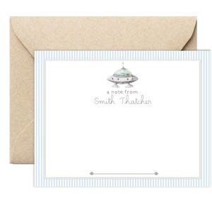 May include: A stationery set featuring a light blue striped card with a watercolor illustration of a UFO and the text "a note from Smith Thatcher." The card is paired with a kraft paper envelope.