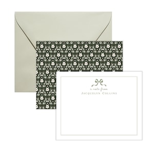 May include: A white card with a green border and a green bow with the text "a note from JACQUELYN COLLINS". The card is on top of a green and white floral patterned card.