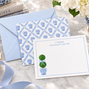 May include: A white stationery card with a blue border, featuring the text 'a note from JACQUELYN COLLINS' and a green topiary in a blue and white patterned pot. It is paired with a light blue envelope with a blue and white patterned liner.