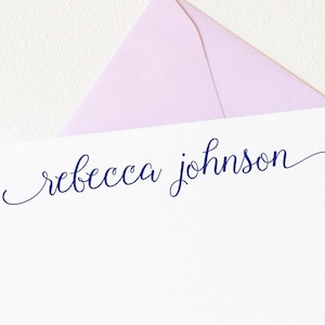 May include: A white card with a light pink envelope on top. The card has the name "rebecca johnson" written in blue cursive.