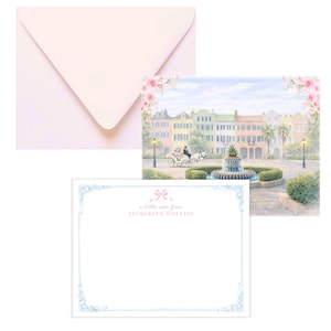 May include: A stationery set featuring a pale pink envelope, a note card with a blue border and the text "a little note from Jacquelyn Collins", and a card with a watercolor painting of a city square.