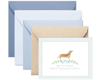 May include: Stationery set featuring a dachshund illustration. The card has a light blue striped border and a watercolor image of a dog with a blue bow and greenery. Includes envelopes in blue and kraft colors. Text reads "from the nursery of Smith Thatcher Collins."
