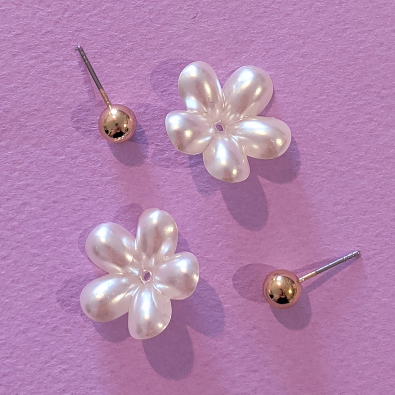 a pair of white flower shaped earrings on a purple background