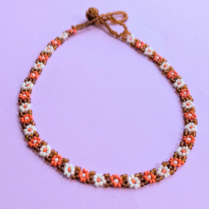 The beaded choker necklace is arranged in a full circle showing its continuous daisy pattern and button closure.