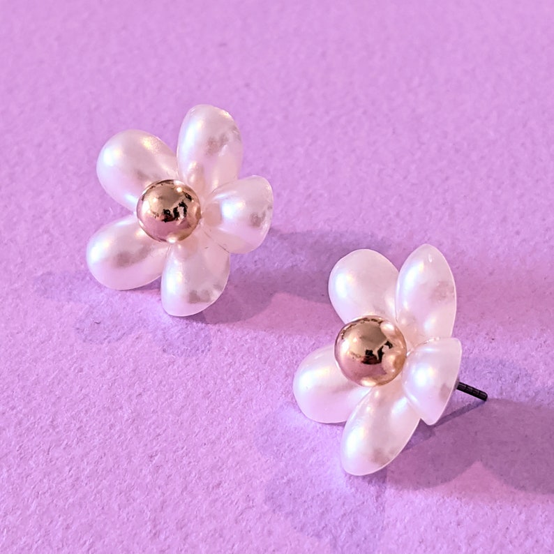 a pair of white flower shaped earrings on a purple background