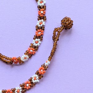 A macro shot focuses on the brown beaded button closure and end loop of the floral choker.
