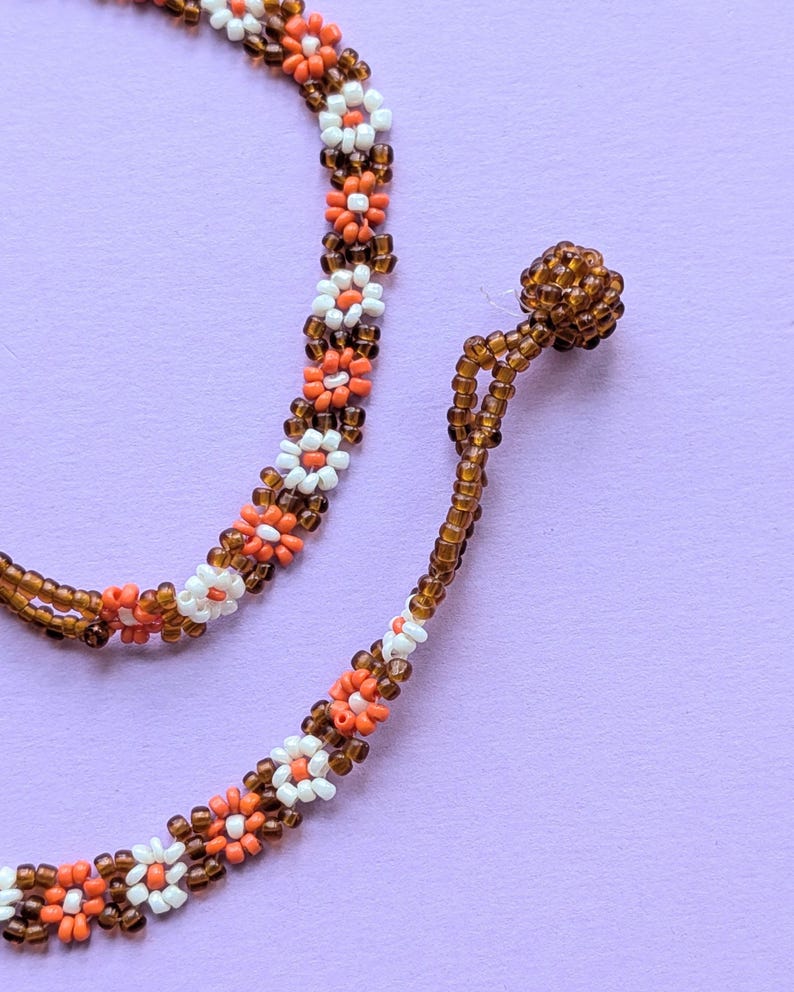 A macro shot focuses on the brown beaded button closure and end loop of the floral choker.