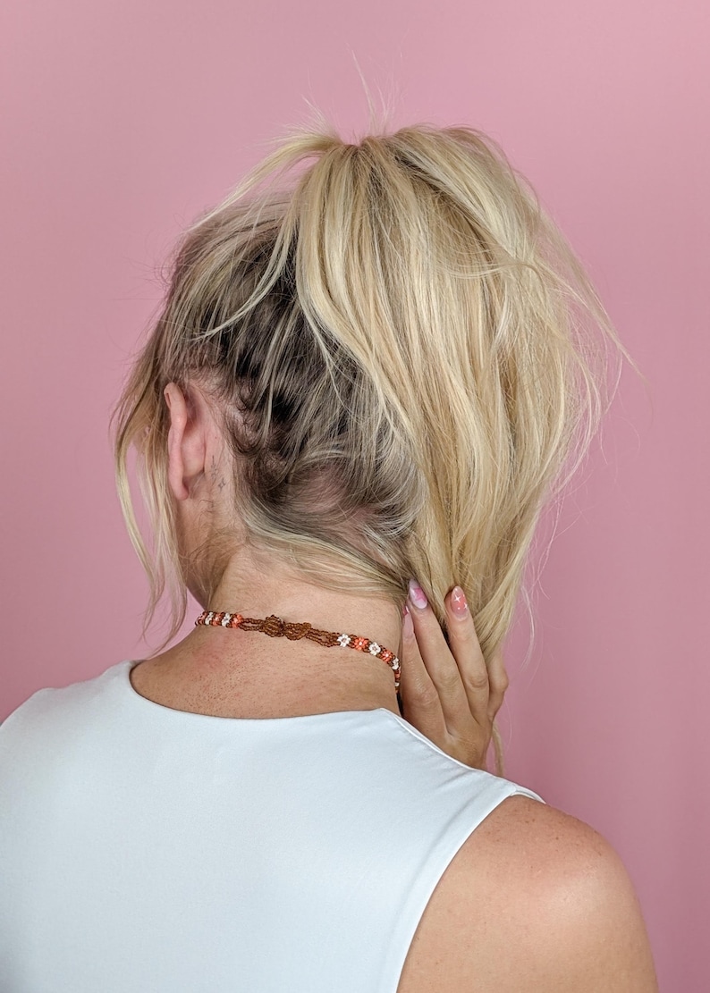 The back of the blonde woman's head shows her ponytail and the clasp area of the choker necklace.