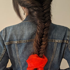 a woman with a fish tail braid in her hair and a red hair bow